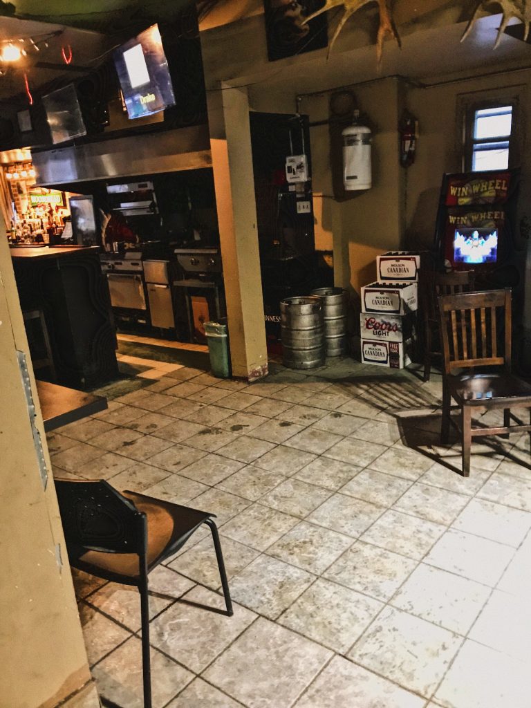 Inside of Dug Out. White tile floor with empty boxes stacked and chairs strewn around.