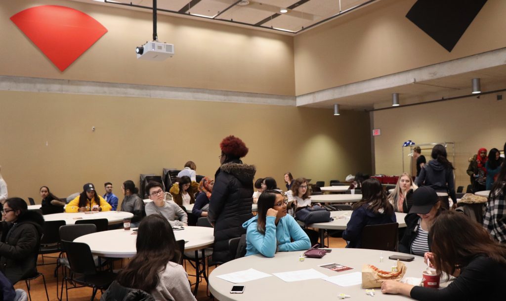 Students and staff sit at tables in the Tecumseh Auditorium.