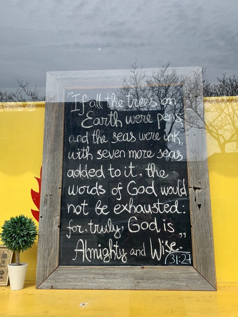 A sign placed in the window of the mosque. It reads, "If all the trees on the earth were pens, and the seas were ink, with seven more seas added to it, the words of God would not be exhausted: for, truly, God is Almighty and Wise." 31:27
