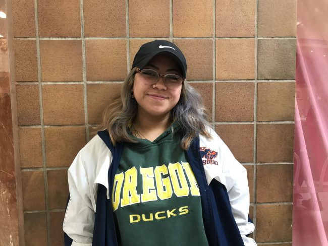 Filipino girl wearing a black hat, white jacket on top of a green sweater that says Oregon Ducks