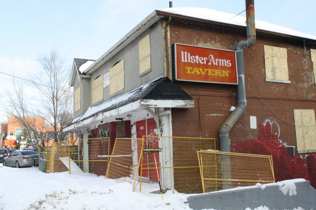 Two-storey house that is boarded up, with a red Ulster Arms Tavern sign