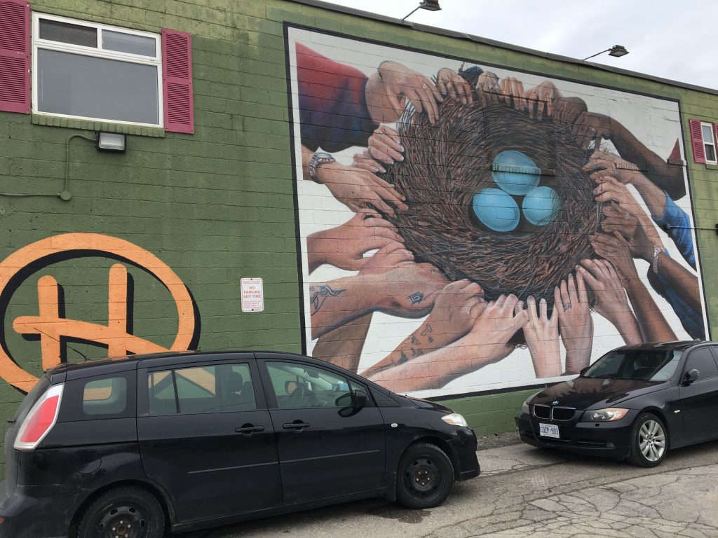 The mural is in the parking lot and has three small robin eggs being supported in a nest by many helping hands.