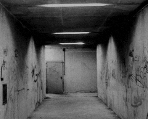 Lights flickering in a dark cement hallway with graffiti on the walls.