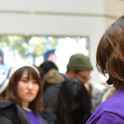A large group of people standing in a tall room. There is one person in focus, and they are staring upwards at something out of shot.