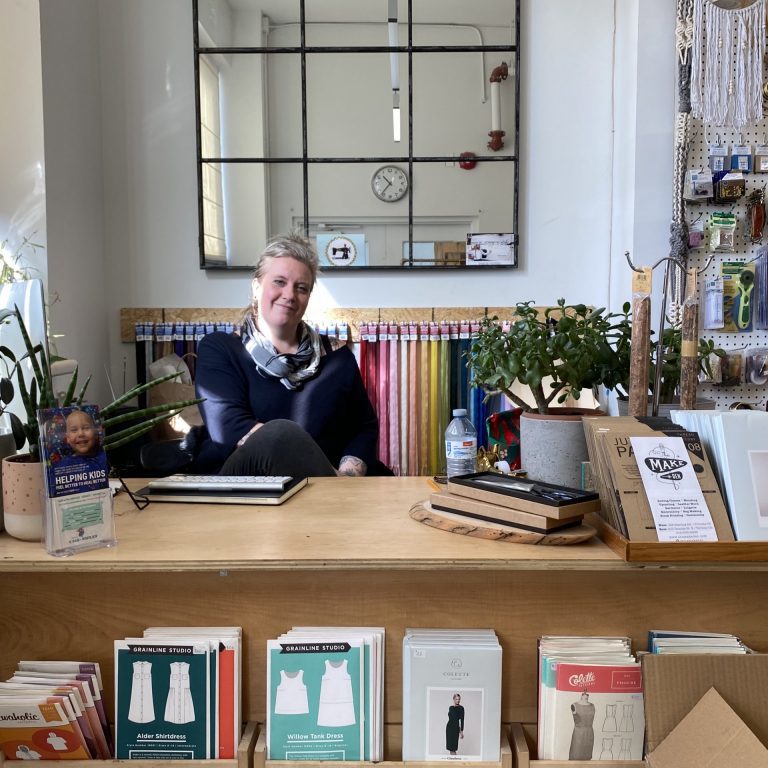 A woman sits at a desk surrounded by craft supplies for purchase