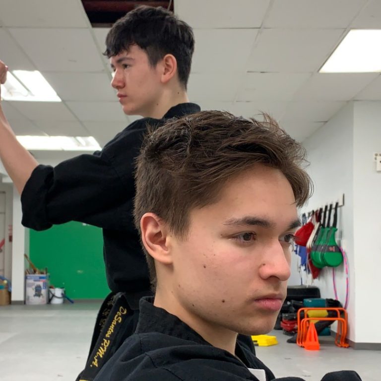 Two people are posed in a fighting stance in a white studio There are workout accessories sitting against a green wall in the background.