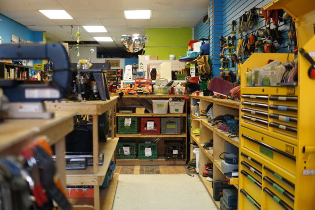 A closeup of a large workbench area. There are plastic bins with tools, saws, and protective equipment.