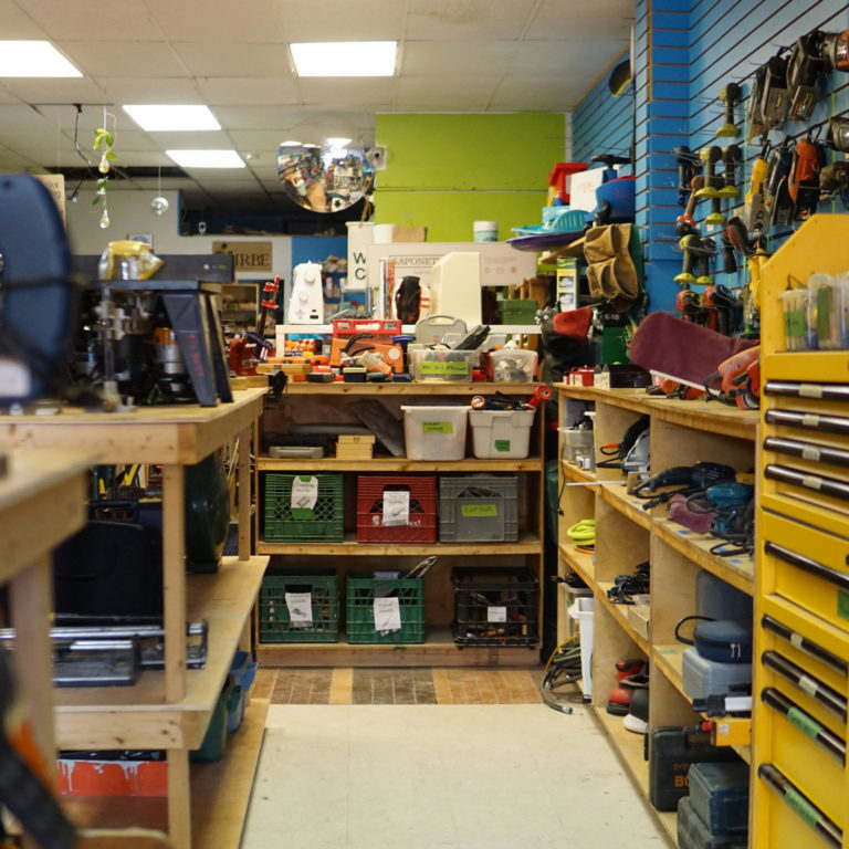 A closeup of a large workbench area. There are plastic bins with tools, saws, and protective equipment.