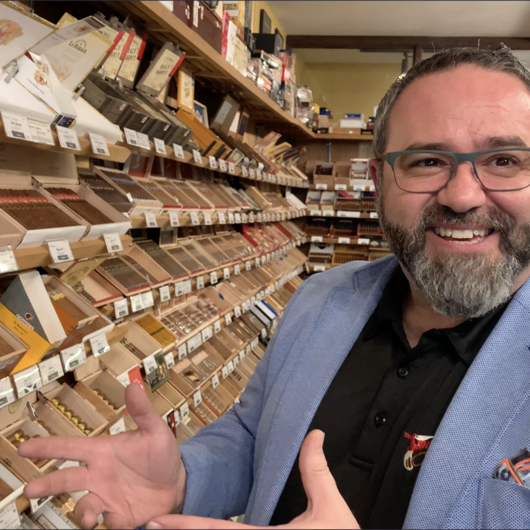 Person with a blue blazer smiling standing in front of shelves of cigars.