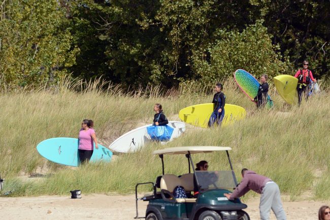 Five people holding surfboards walking down towards a beach.