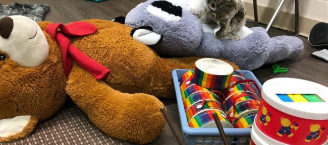 Children's toys lying on the ground. There are stuffed toys, drum sets, and art supplies.