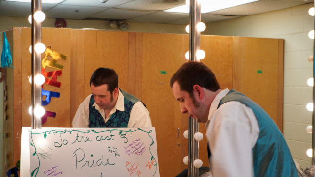 Person in a white top and teal vest in front of a mirror.