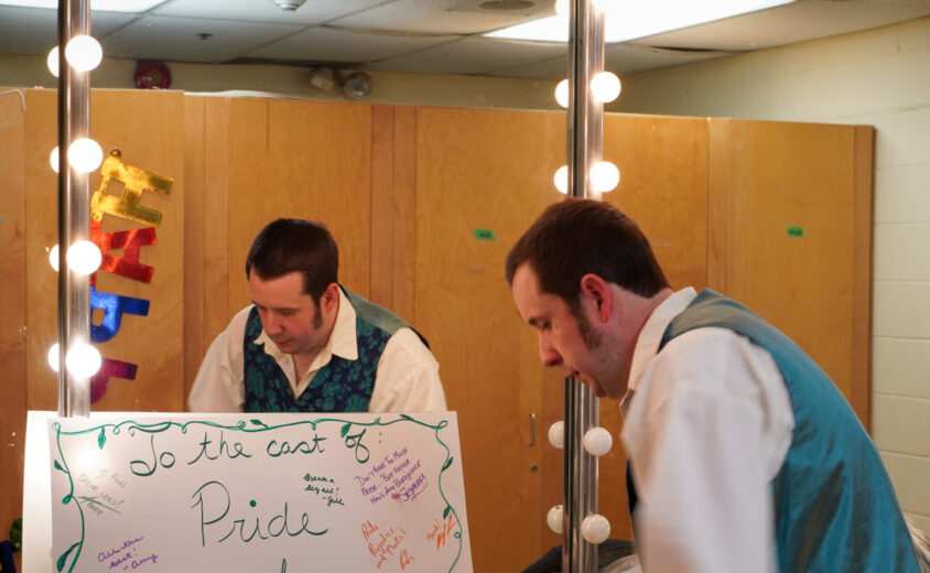 Person in a white top and teal vest in front of a mirror.