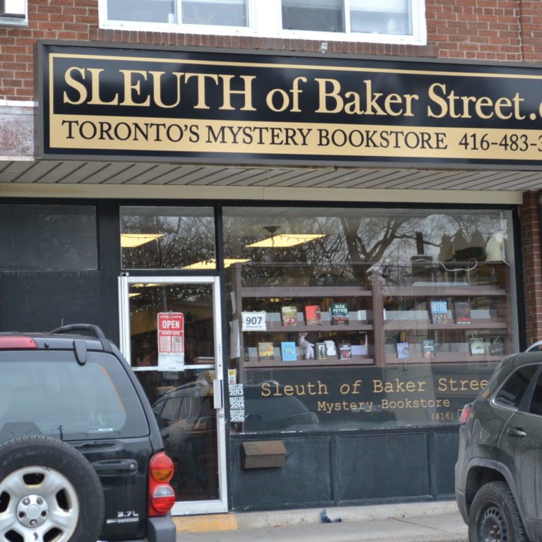 The exterior of the sleuth of baker street store. The building is brown brick, with the storefront frame painted black.