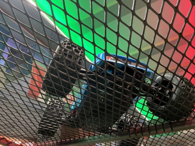 Upwards angle of the underside of a toy car through a metal grate.