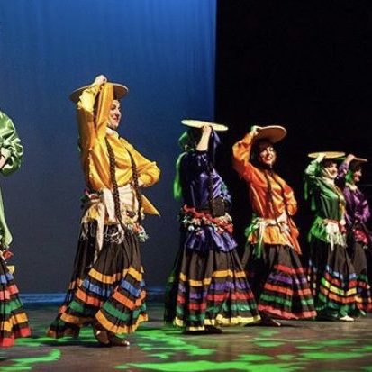 IMG_0082 Women dancing onstage in silk shirts and brightly coloured skirts. They're holding wicker baskets on top of their heads.