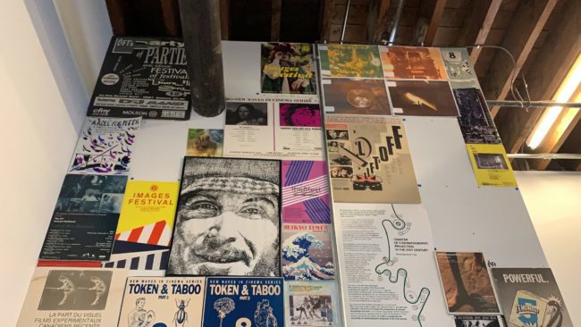 Wall decorated with posters. The posters all have varying aesthetics and advertise different things, although they are purely decorative now.