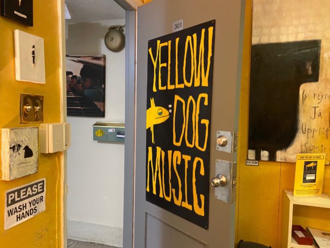 Silver door with a giant poster that says yellow dog music on it. The surrounding walls are yellow.