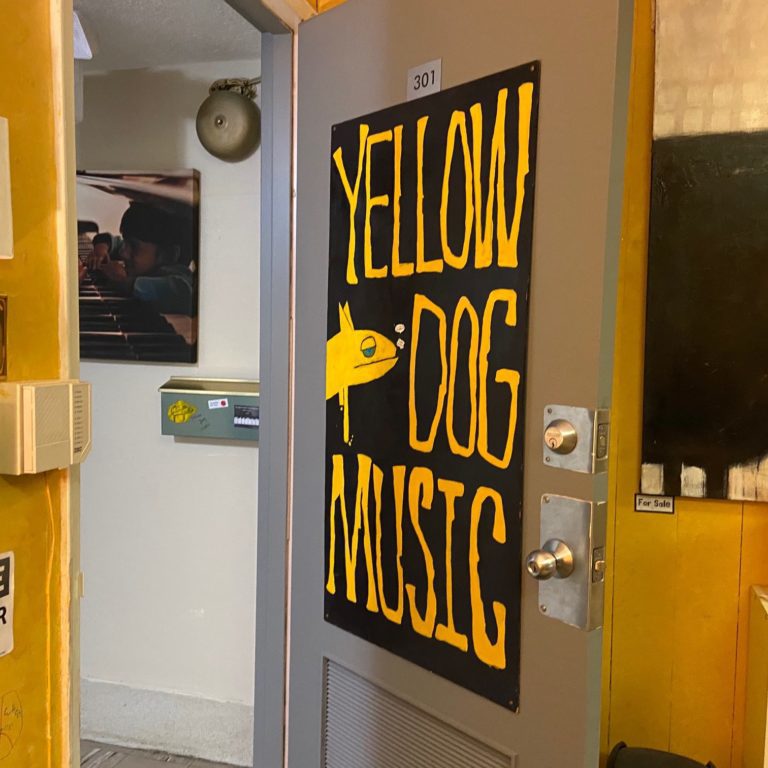 IMG_1389 Silver door with a giant poster that says yellow dog music on it. The surrounding walls are yellow.