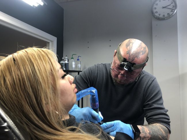 Person tattooing another person.