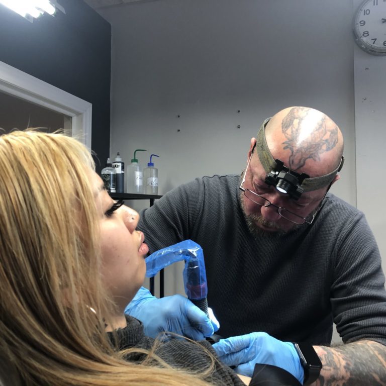 Person tattooing another person.
