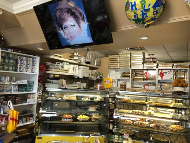 the interior of a bakery. The shelves are filled with various chocolates and baking ingredients, while the glass shelves in front have several baked goods sitting out for purchase.