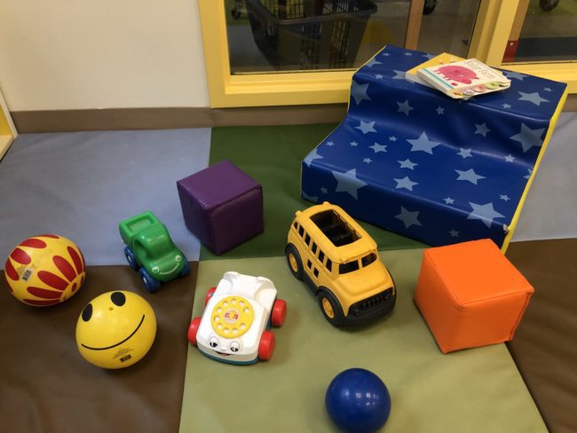 children's toys on a multicoloured mat. small cars, balls, and books are all present.