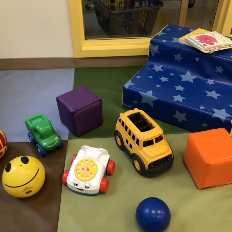 children's toys on a multicoloured mat. small cars, balls, and books are all present.