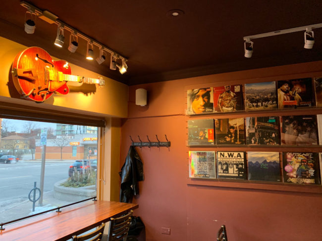 Sitting area with a guitar on the wall. There is also a wall of Vinyl CD cover art.