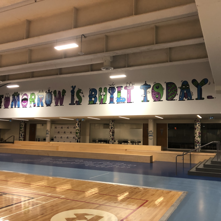 Gym floor and bleachers. The sign above the bleachers says tomorrow is built today in blue, green, and purple animated letters.