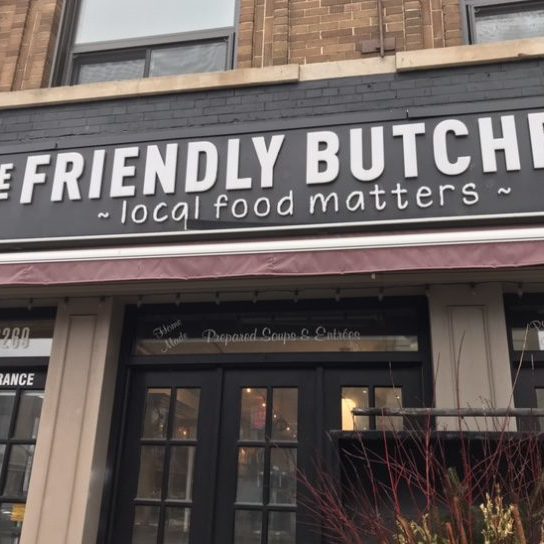 A street image of The Friendly Butcher storefront. Inside there are several lights on.