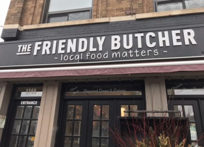 A street image of The Friendly Butcher storefront. Inside there are several lights on.