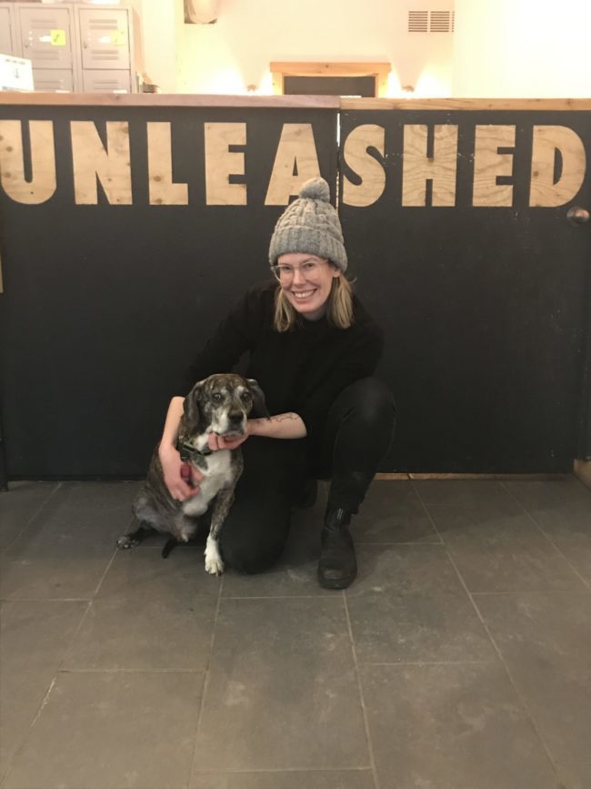 Woman kneeling beside a small dog under a sign that says unleashed.