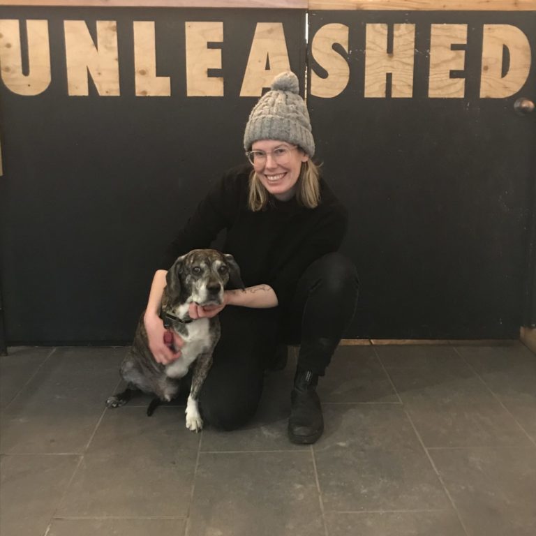 Woman kneeling beside a small dog under a sign that says unleashed.