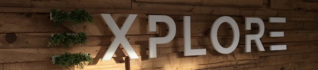 a banner image of the explore printing logo. The background wall is wood panelling, and the 'e' in explore is filled with succulents.