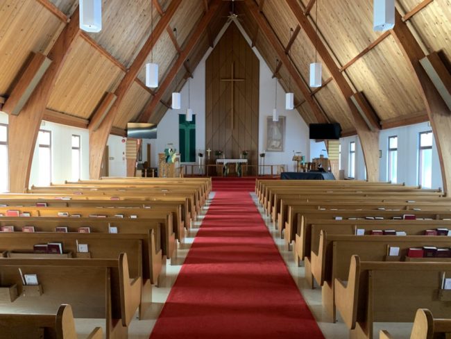 Empty church pews, a red carpet on the floor, nature lighting through the aisles