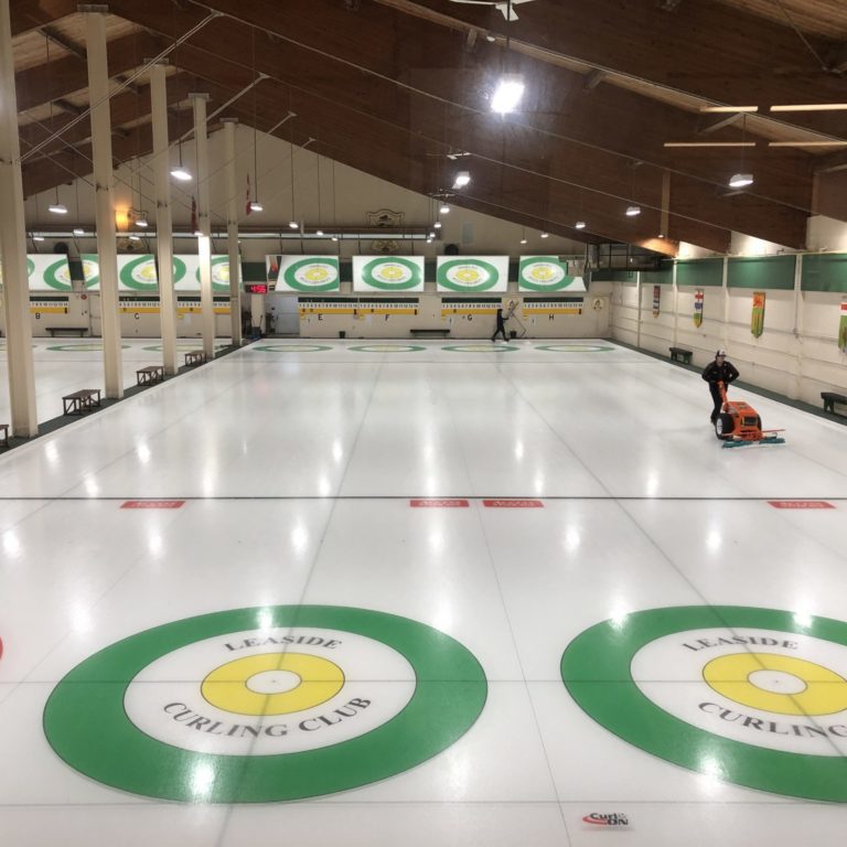 Indoor curling arena with two people cleaning.