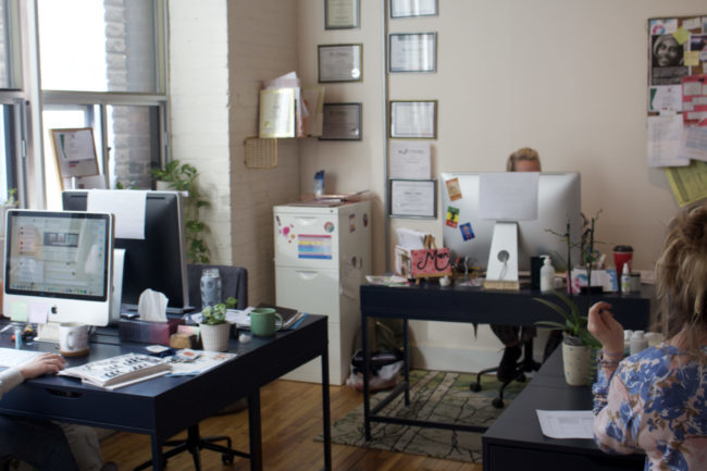 Work office that has four desks and four desktop computers. The room has colourful decorations and hanging photos.