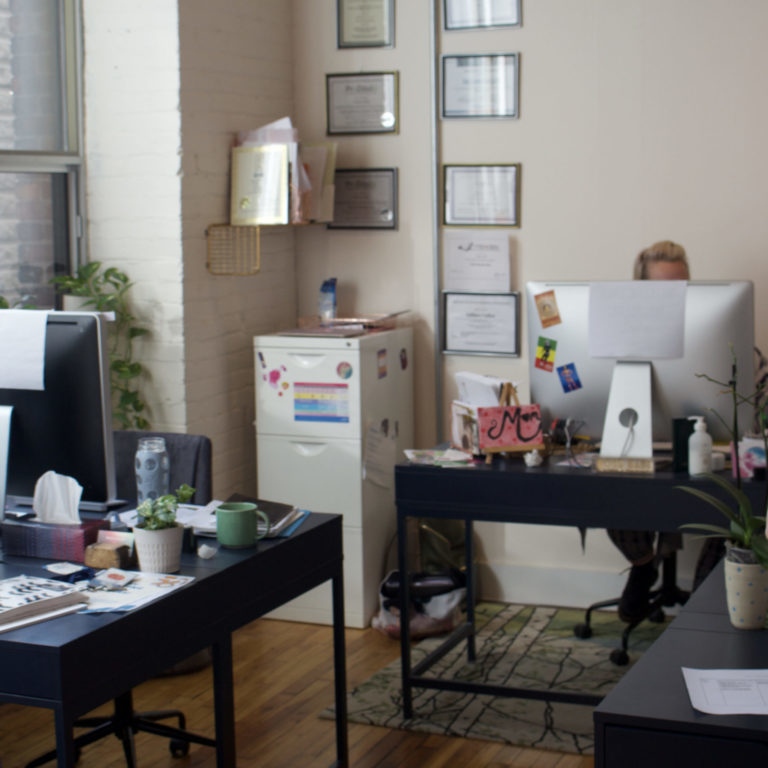 IMG_9778 copy Work office that has four desks and four desktop computers. The room has colourful decorations and hanging photos.