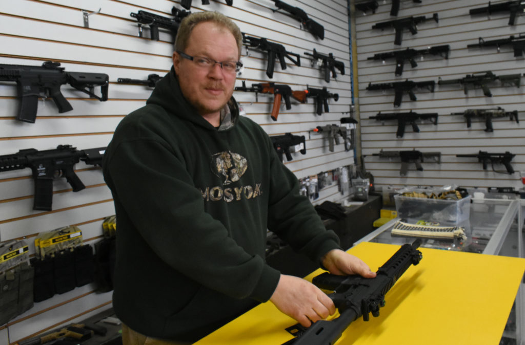 A man with an airsoft rifle on a yellow sheet of plastic board.
