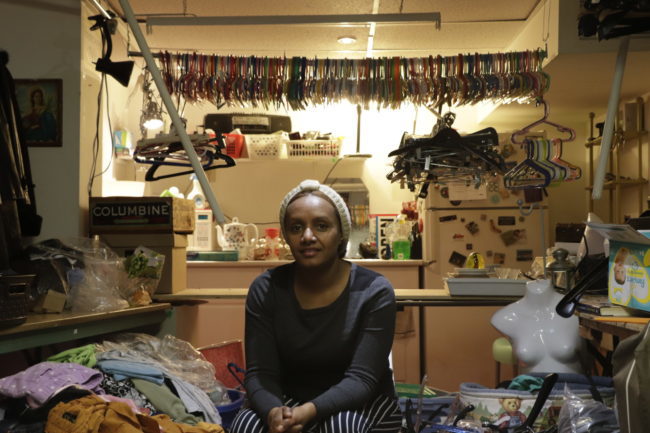 Person sitting next to a pile of clothes. Behind her are thousands of clothes hangers.