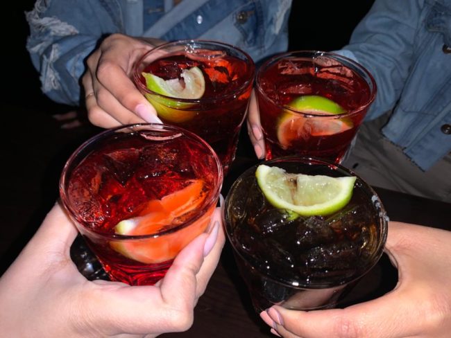 People holding drinks with limes in them. The background is dark as though the image has been taken with flash.