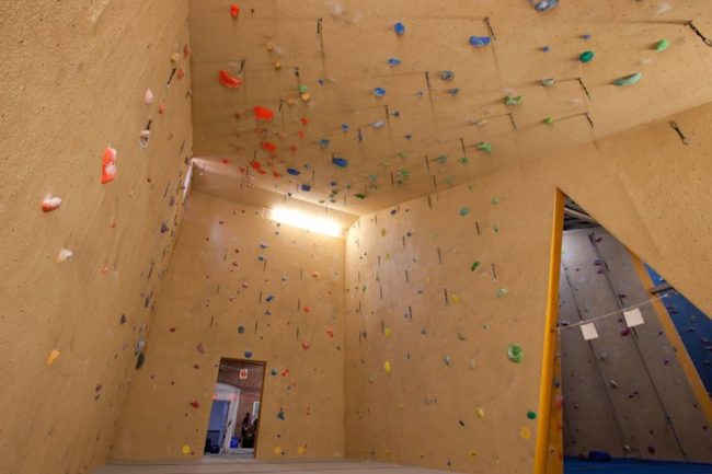 A concrete room is covered in small foot handles for indoor rock climbing. The hooks are also attached to the ceiling, giving lots of options on where to climb.