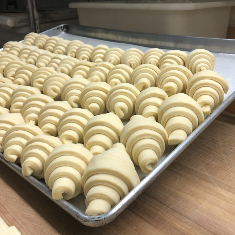Large tray of uncooked croissants sitting on a piece of parchment paper.