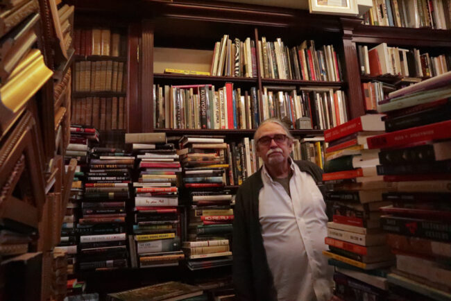 Man standing in a bookstore with piles of books.