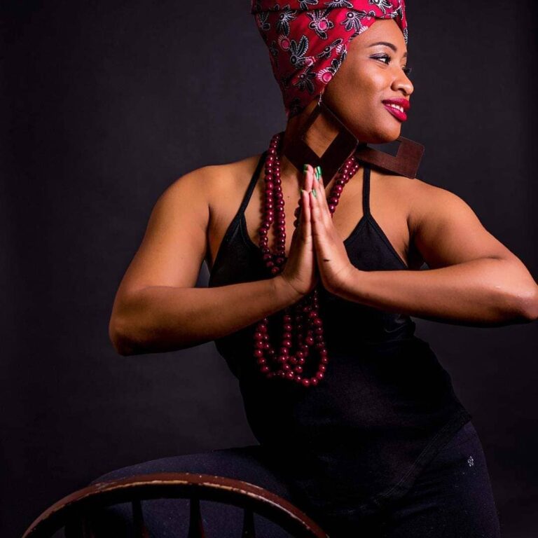 Woman with her hands to her chest in a yoga pose while looking away from the camera.