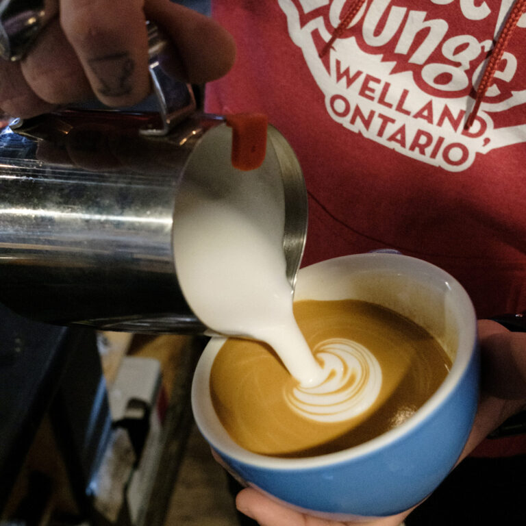 Person pouring cream into a cup of coffee.