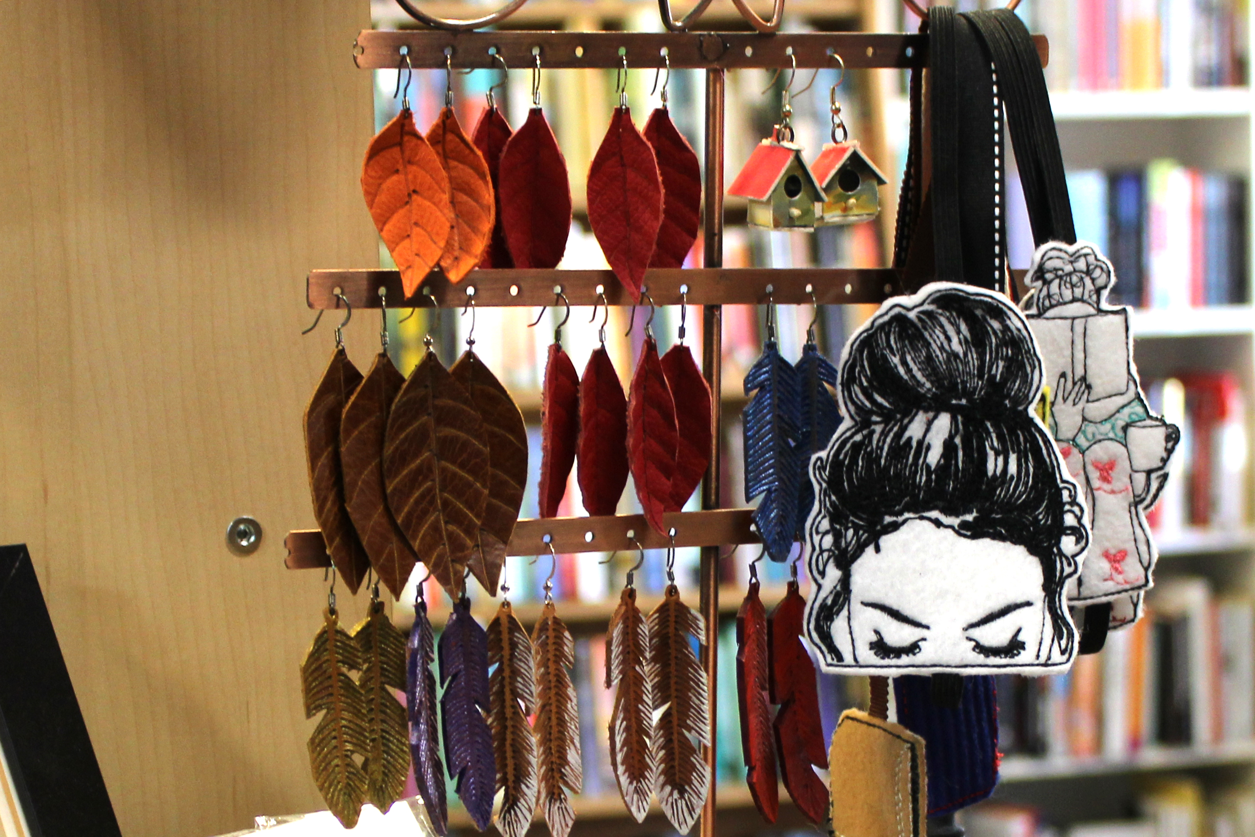 Jewelry tree displaying feather-shaped leather earrings. A bookmark of a girl reading dangles off the side.