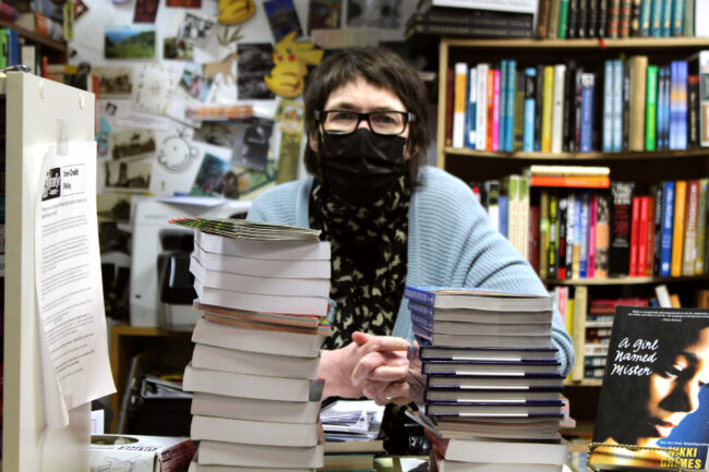 Person standing behind two tall stacks of books.