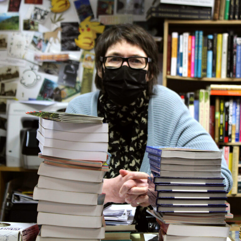 Person standing behind two tall stacks of books.